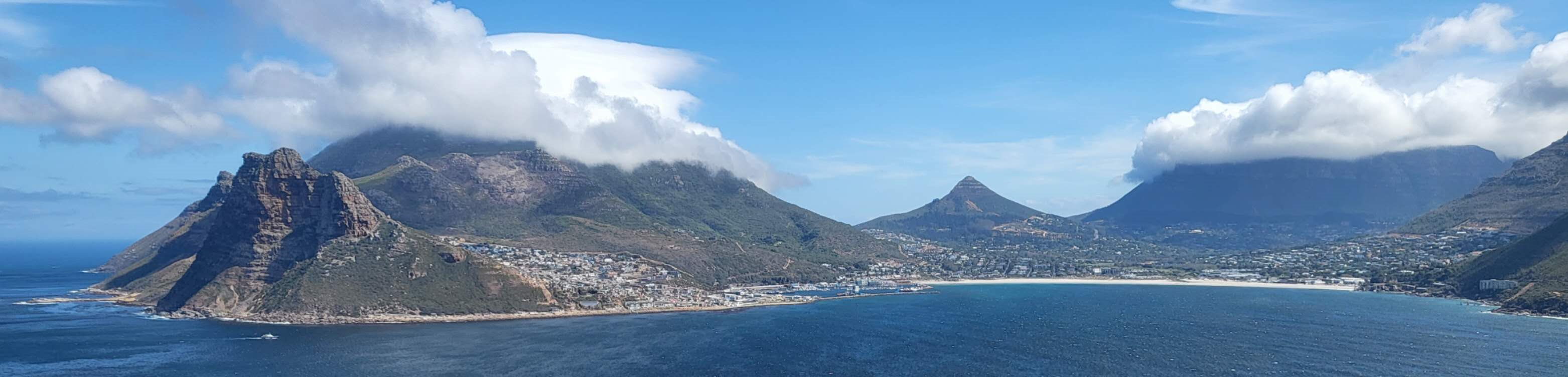 A wide coastal landscape with mountains, a bay and a city beneath the clouds